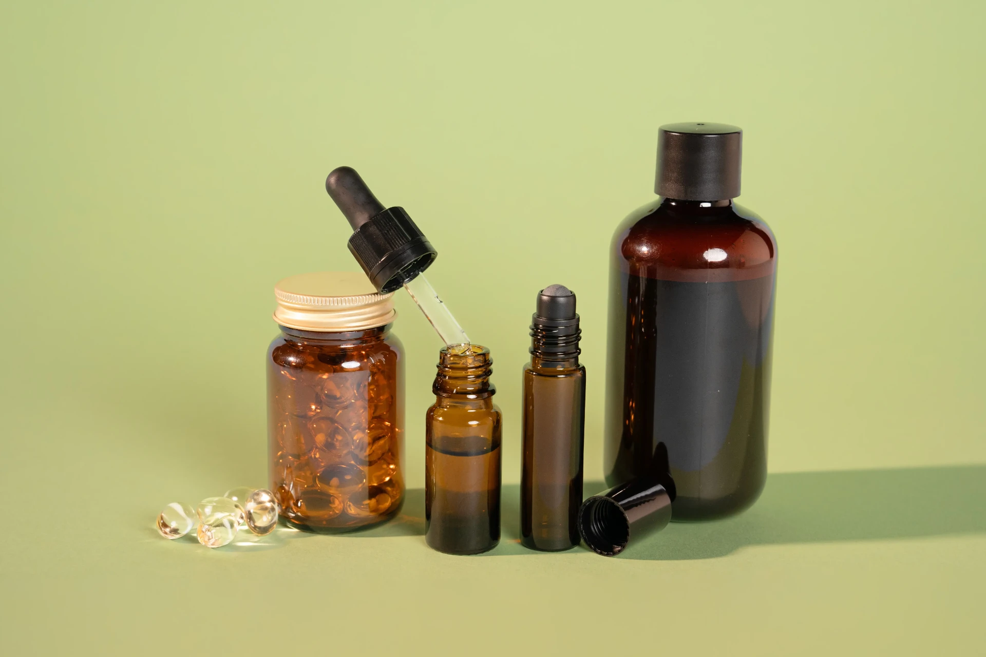 Contenitori in vetro ambrato per integratori su fondo verde: barattolo di capsule con capsula dorata, flacone con contagocce, roll-on e flacone con tappo nero