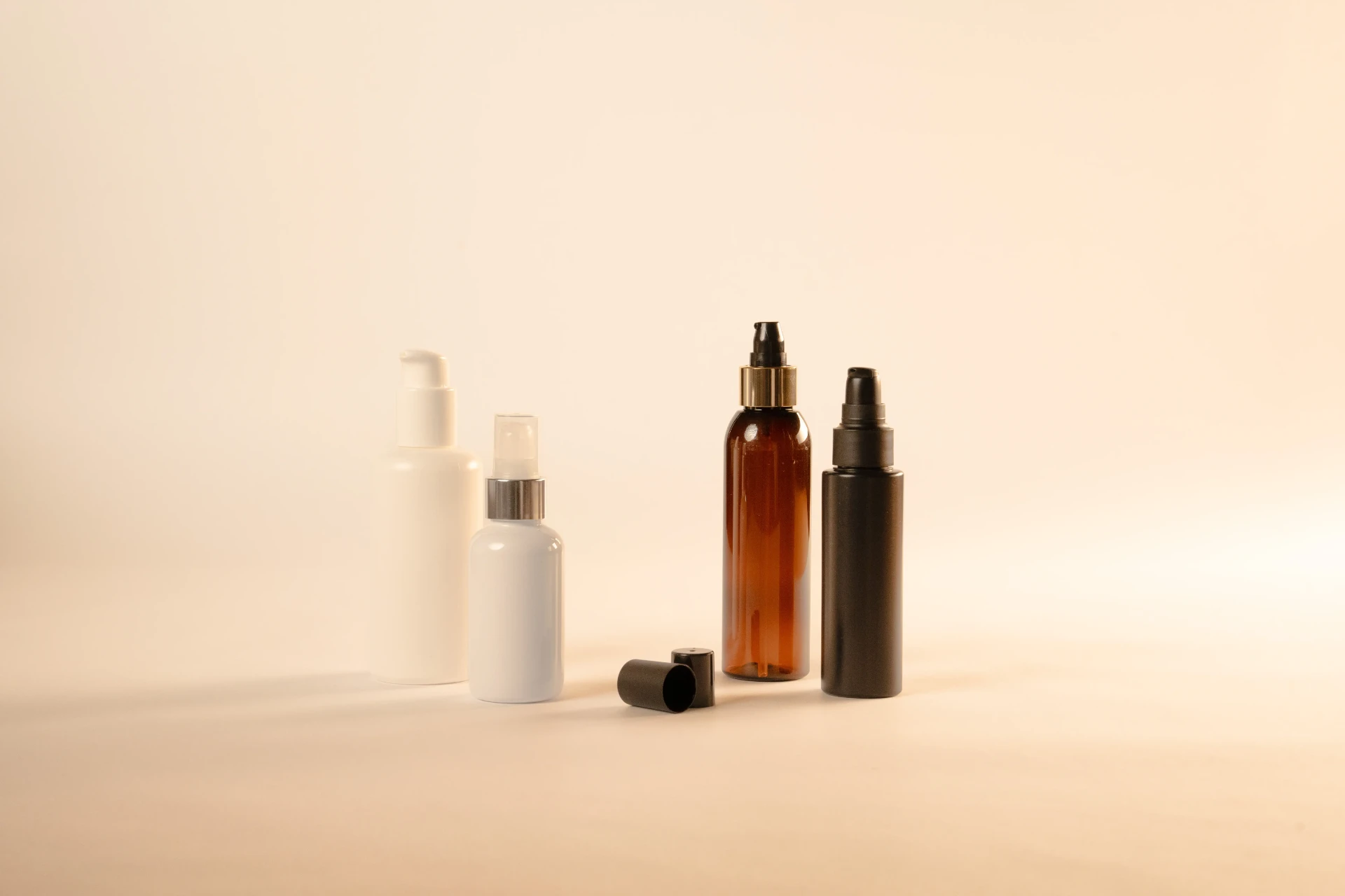 Quattro flaconi con dosatori a pompa: bianco, spray con ghiera argentata, ambrato con ghiera dorata e nero