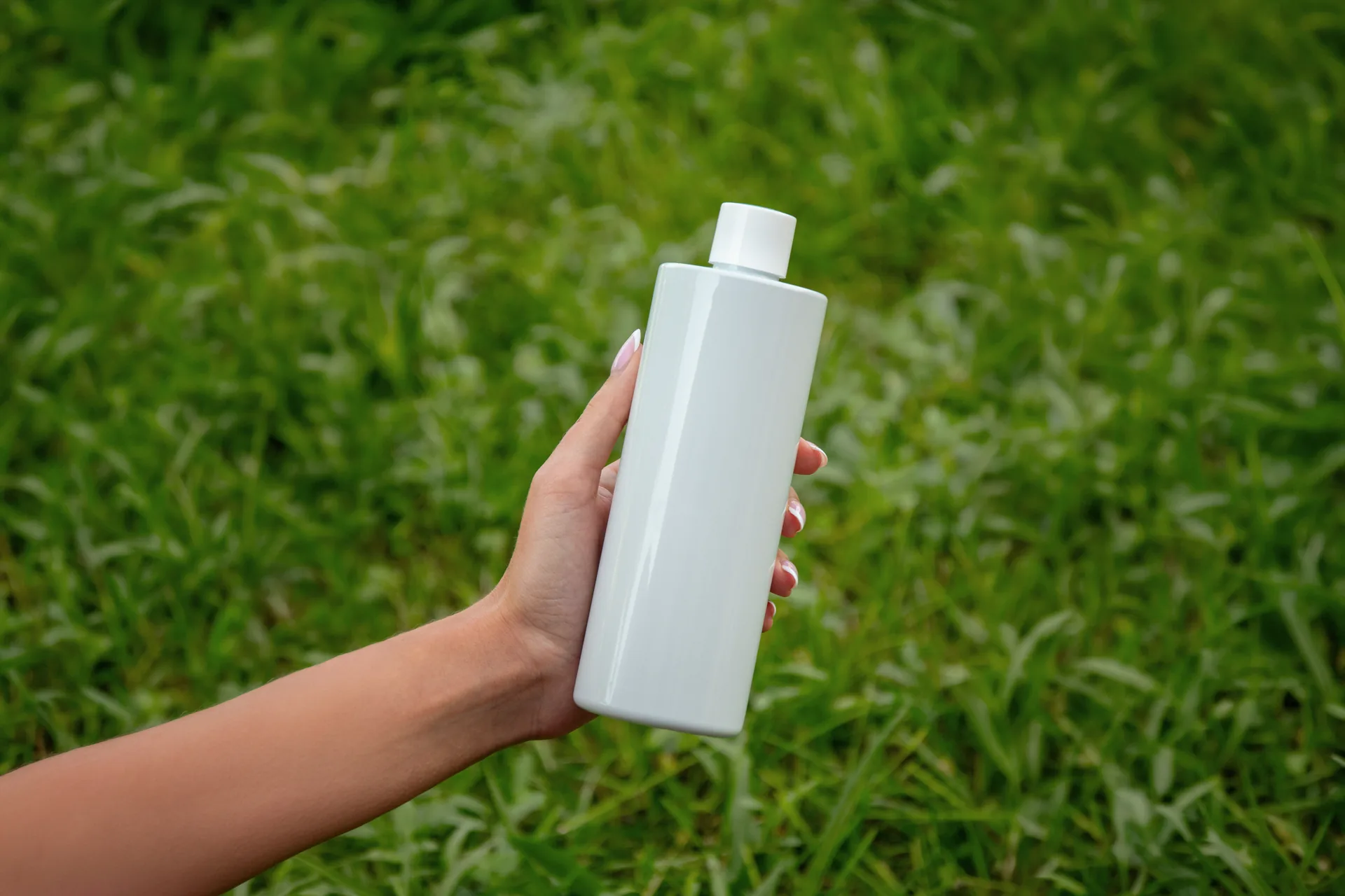 Mano che tiene un flacone in plastica riciclata sopra un prato