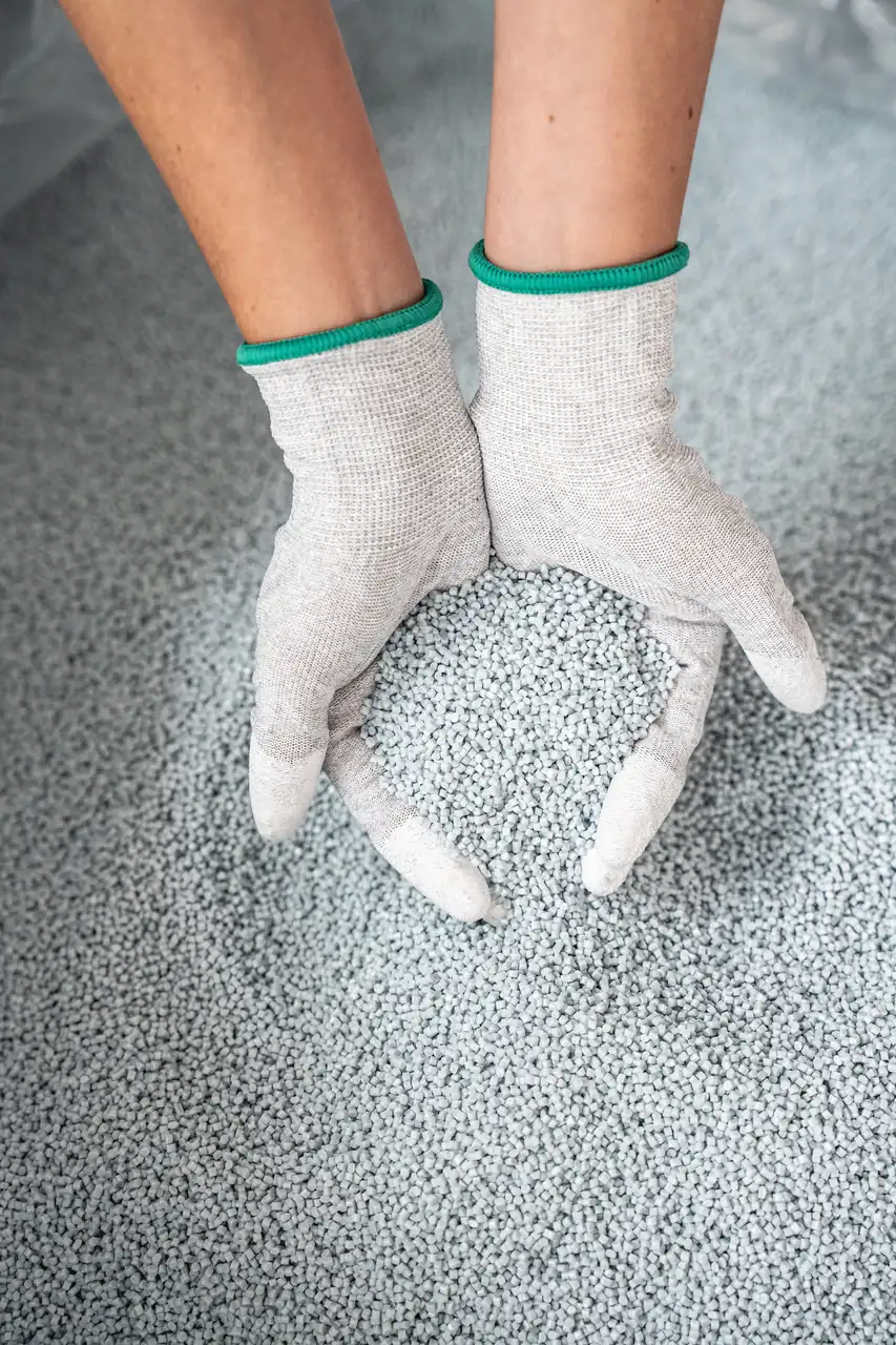 Mani con guanti che raccolgono granuli di plastica riciclata
